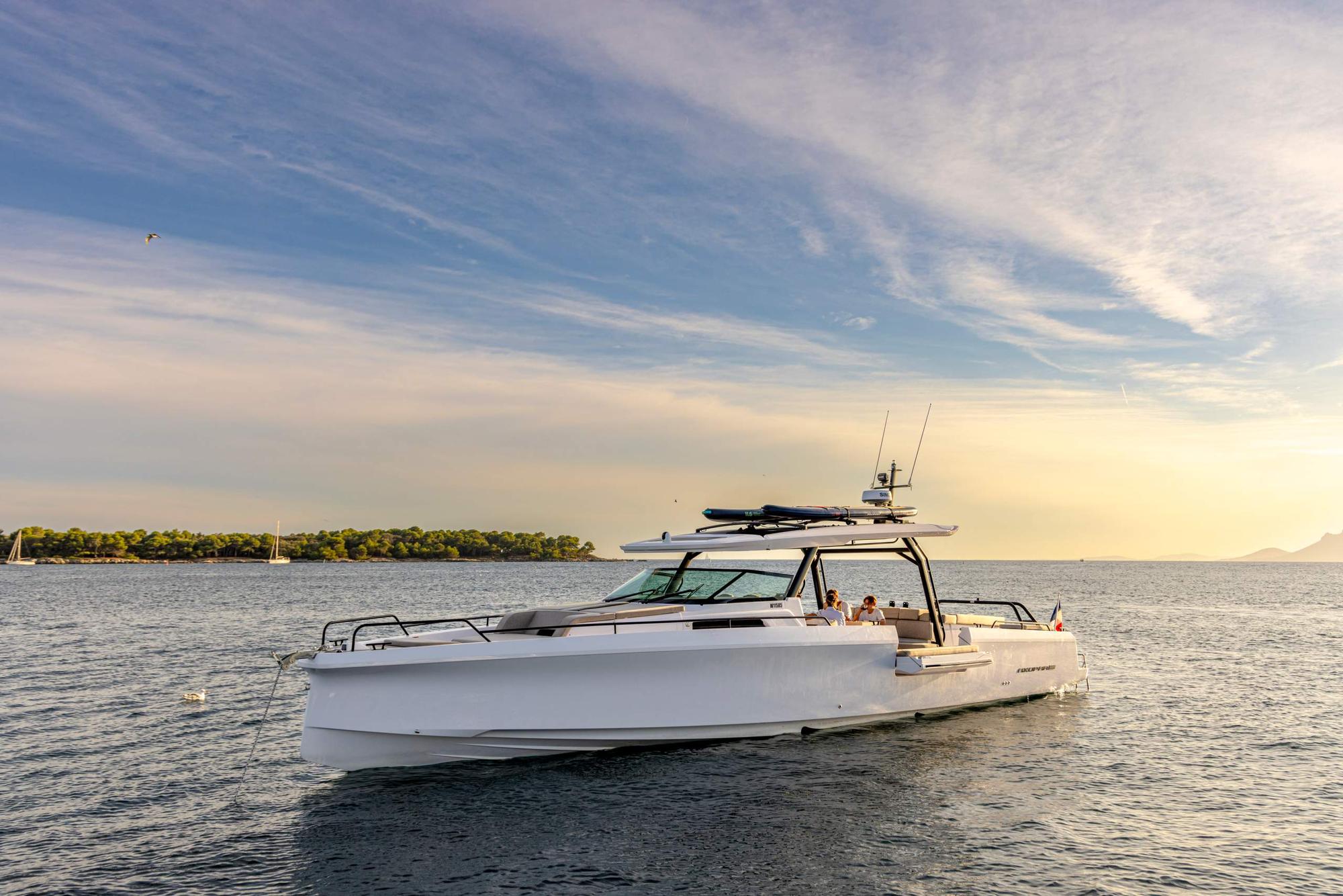 Bateau Axopar au mouillage à l'heure dorée près d'un îlet boisé en Martinique, deux personnes à bord